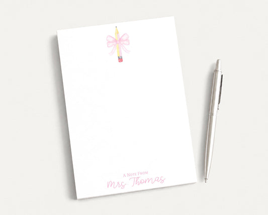 A blank white notepad with a pink bow and a pen on a white surface.