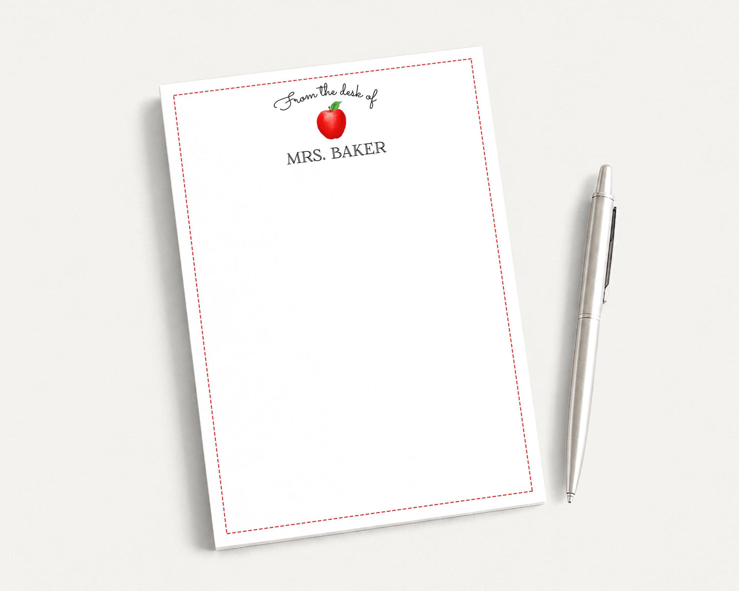A white notepad with a red border and an apple graphic, along with a pen, are placed on a white surface.