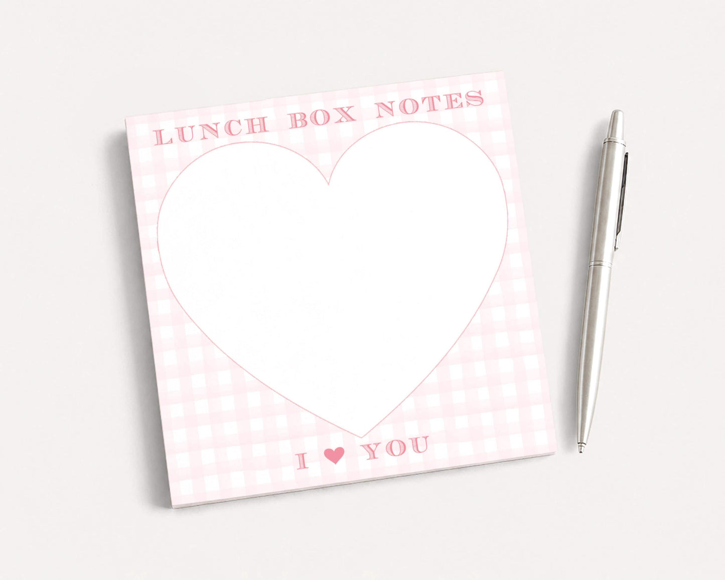 a pink and white checkered lunch box with a heart-shaped blank space and the text "I ❤ YOU" written on it. Next to the lunch box is a pen, suggesting it is a stationery item.