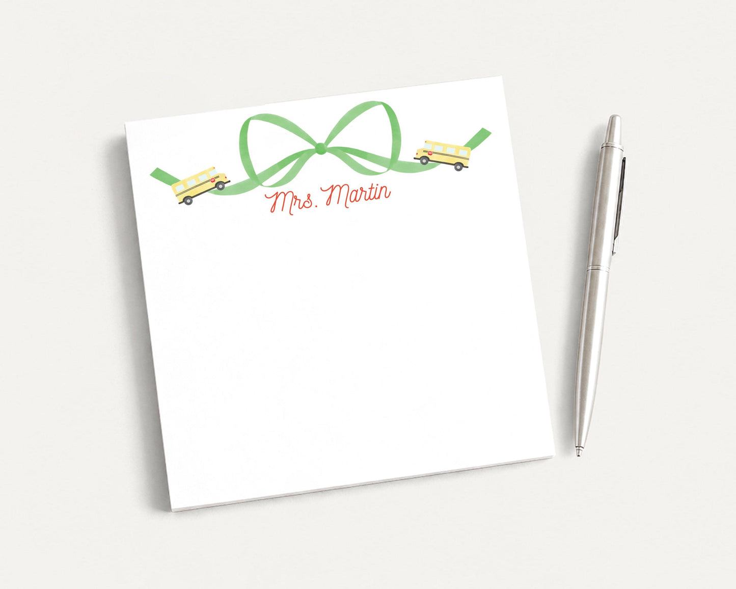 A white notepad with a green ribbon and a pen on a white surface.