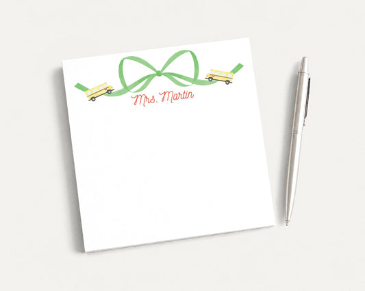 A white notepad with a green ribbon and a pen on a white surface.
