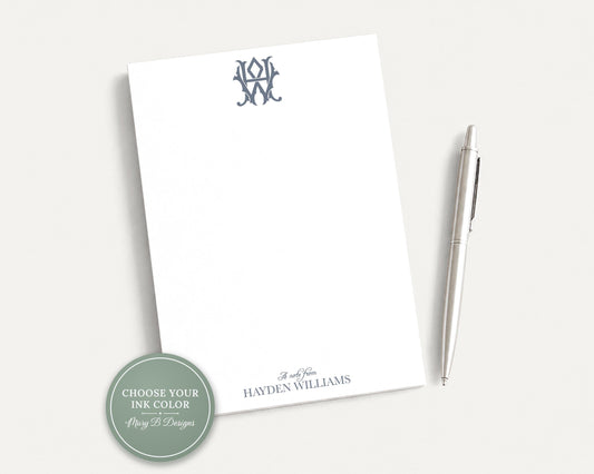 a white notepad with a monogrammed logo and a pen on a plain white surface.