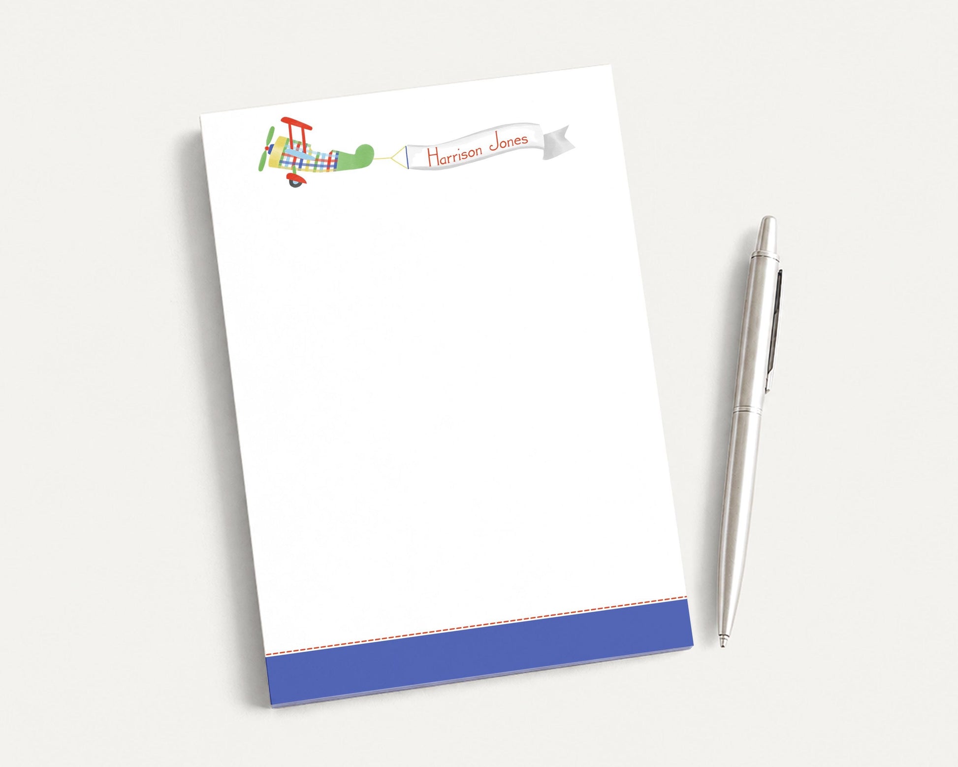 a blank white notepad with a colorful airplane illustration on the top left corner, and a pen is placed next to it on the right side.