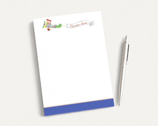 a blank white notepad with a colorful airplane illustration on the top left corner, and a pen is placed next to it on the right side.