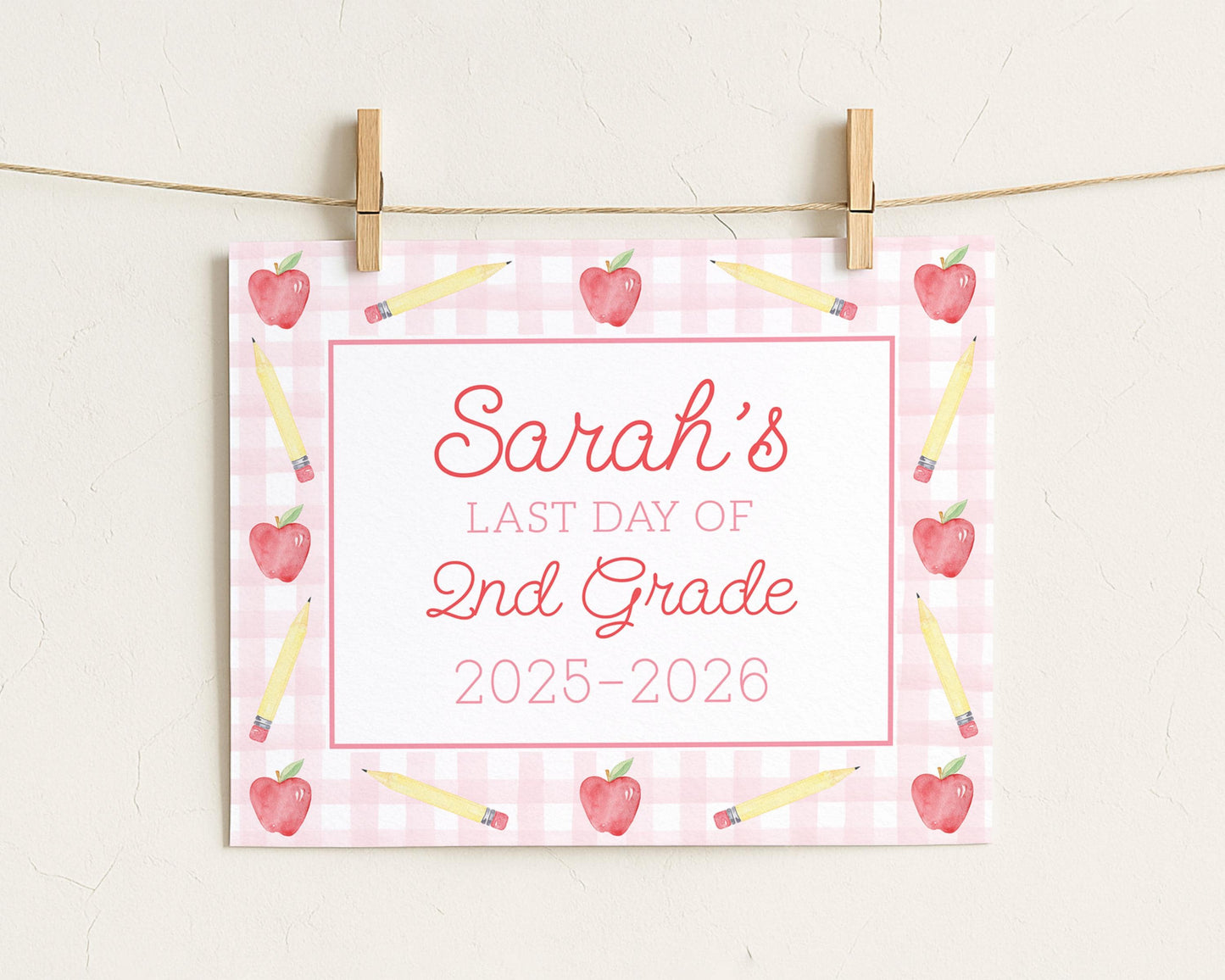 A pink and white sign with the text "Sara's Last Day of 2nd Grade" and illustrations of pencils and apples.