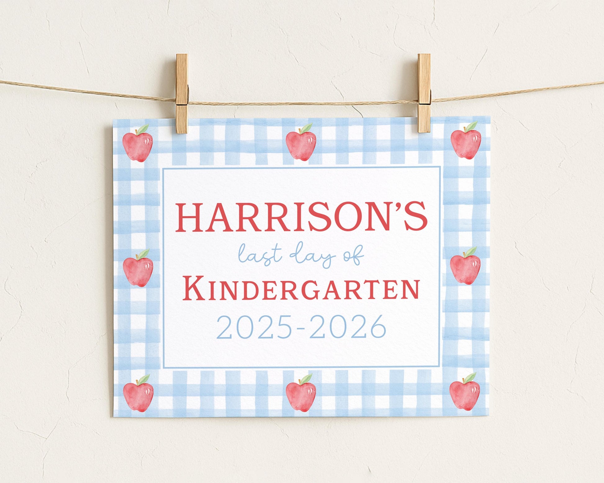 A sign with the text "HARRISON'S last day of KINDERGARTEN" and "2025-2026" printed on it, with a blue and white checkered background and red apples.