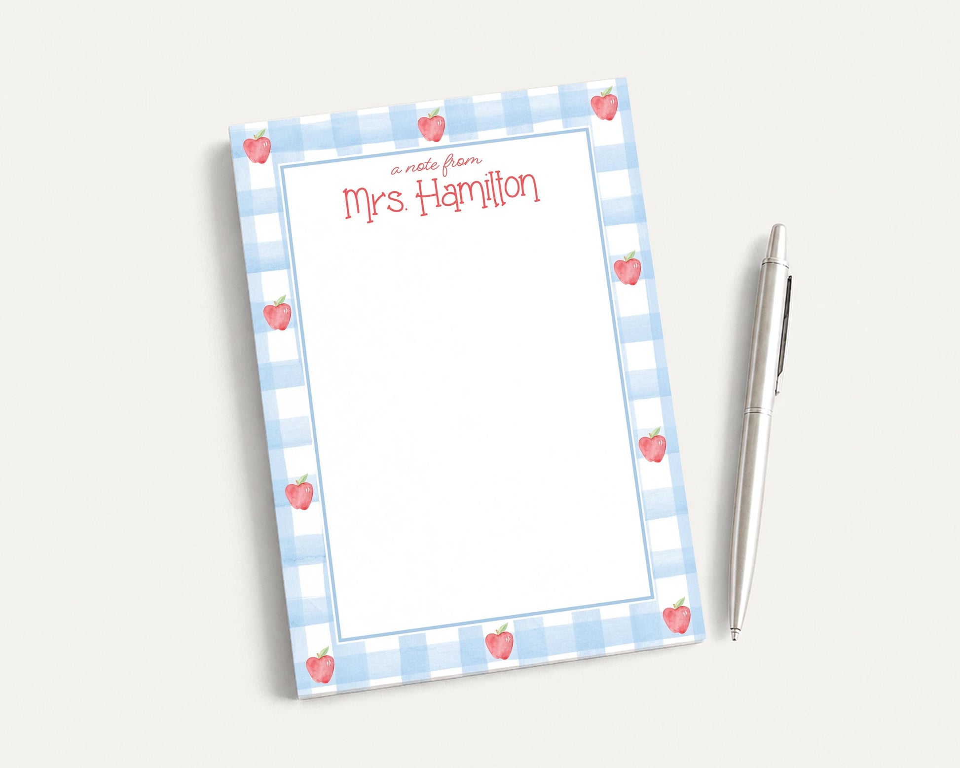 A blue and white checkered notepad with a blank page and a pen on a white surface.