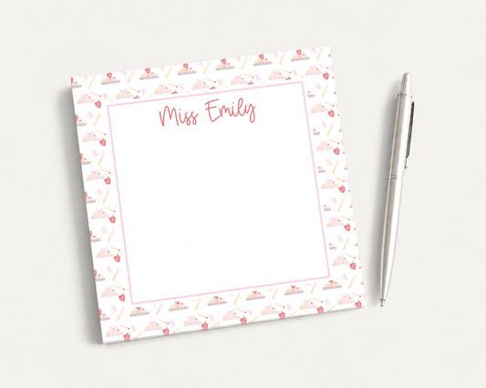 A personalized notepad with a pink and white patterned border, featuring the name "Miss Emily" written in cursive. The notepad is accompanied by a pen, suggesting it is ready for use.