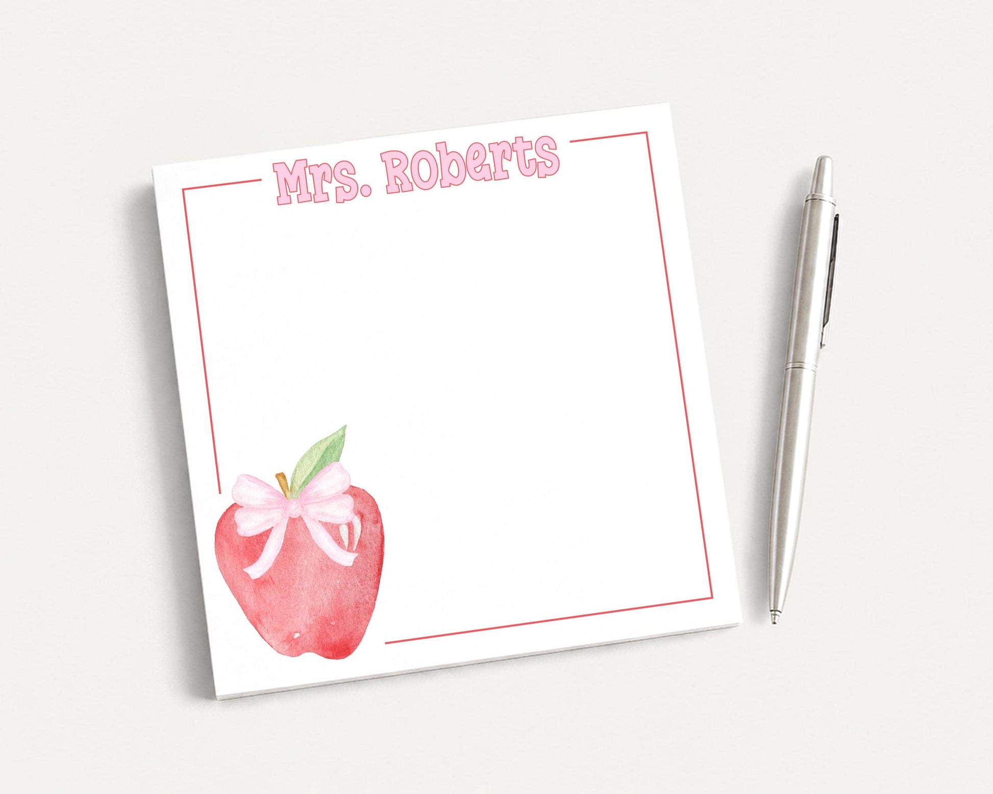a white sticky note with a pink bow on it, placed next to a pen on a white surface.