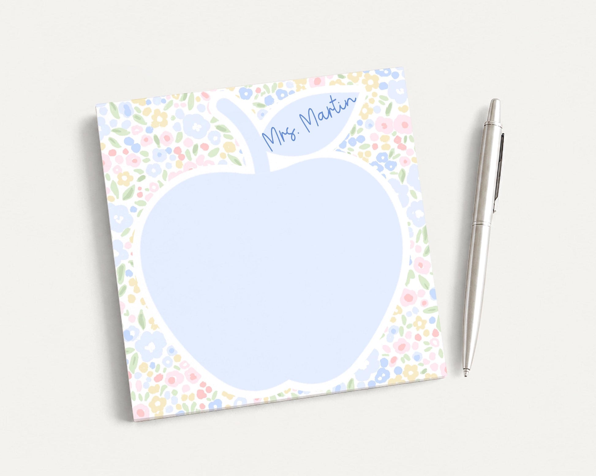 A blue flower-patterned notepad with a blank space in the center, accompanied by a silver pen on a plain white background.