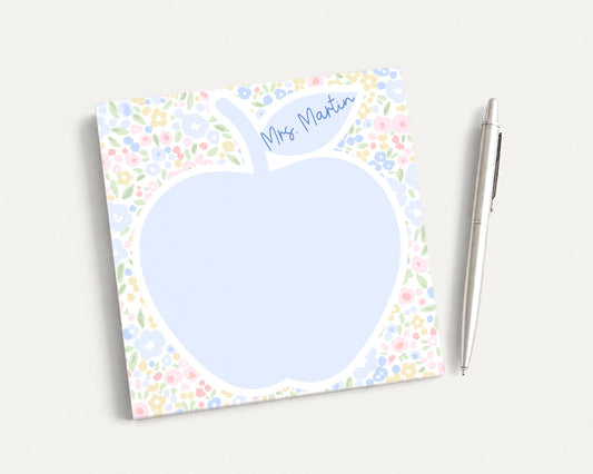 A blue flower-patterned notepad with a blank space in the center, accompanied by a silver pen on a plain white background.
