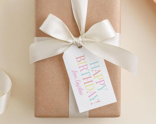 A brown gift box with a white ribbon and a personalized birthday tag attached to it.