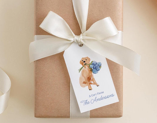 A gift wrapped in brown paper with a white ribbon and a tag featuring a picture of a dog holding a bouquet of flowers.