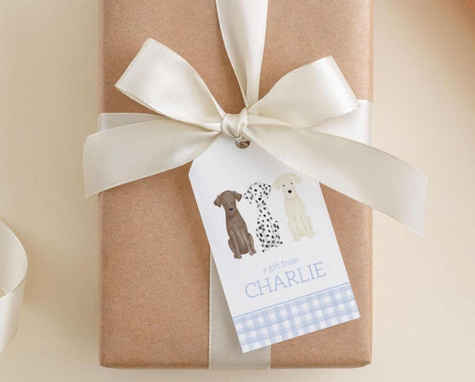 A brown gift box with a white ribbon and a tag featuring illustrations of a brown dog, a white dog, and a black and white dog.