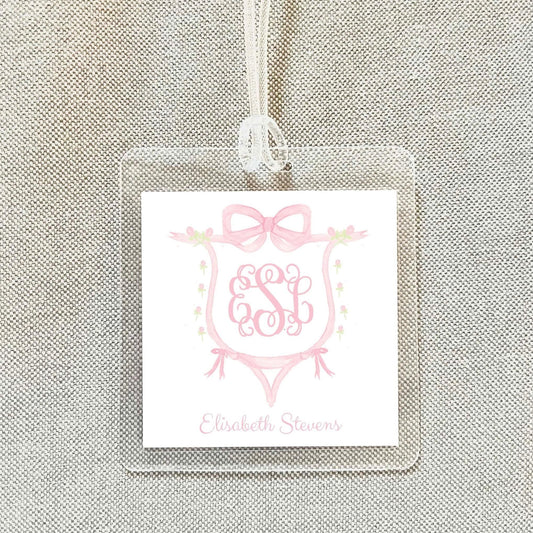 A clear plastic luggage tag with a pink monogram design and the name "Elisabeth Stevens" printed on it.