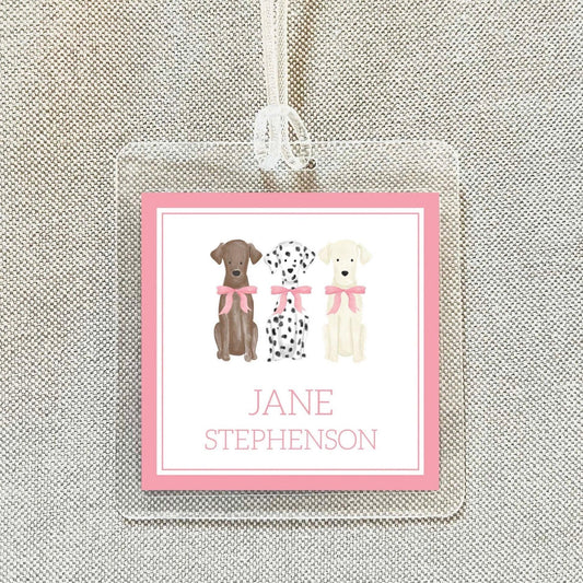 A pink name tag with a picture of three dogs, each wearing a pink bow, and the name "Jane Stephenson" written below.