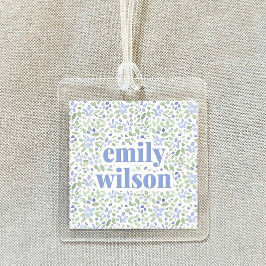 A clear plastic name tag with a floral pattern and the name "emily Wilson" printed on it.