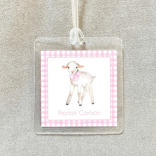 A clear name tag with a pink and white checkered border, featuring an illustration of a lamb wearing a bow tie.