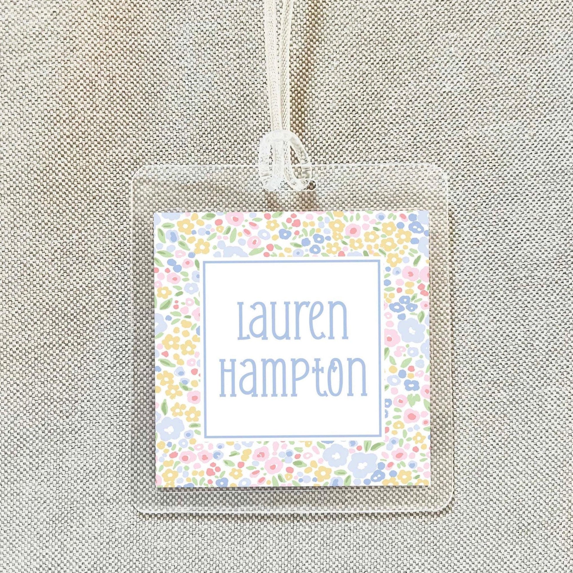 A clear plastic name tag with a floral design and the name "Lauren Hampton" printed on it.