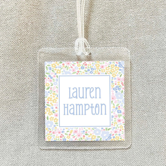 A clear plastic name tag with a floral design and the name "Lauren Hampton" printed on it.