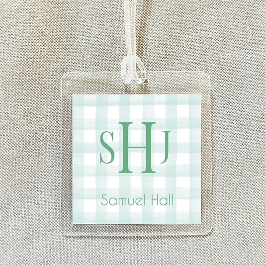 A clear plastic name tag with a green and white checkered pattern and the initials "SHJ" printed on it.