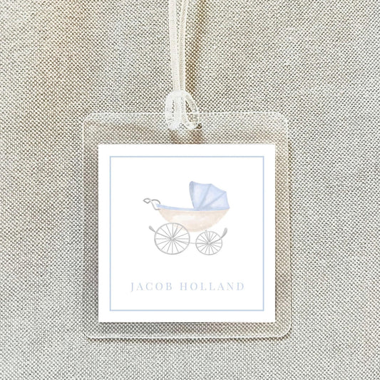 A clear plastic name tag with a blue and white illustration of a baby carriage and the name "Jacob Holland" printed on it.