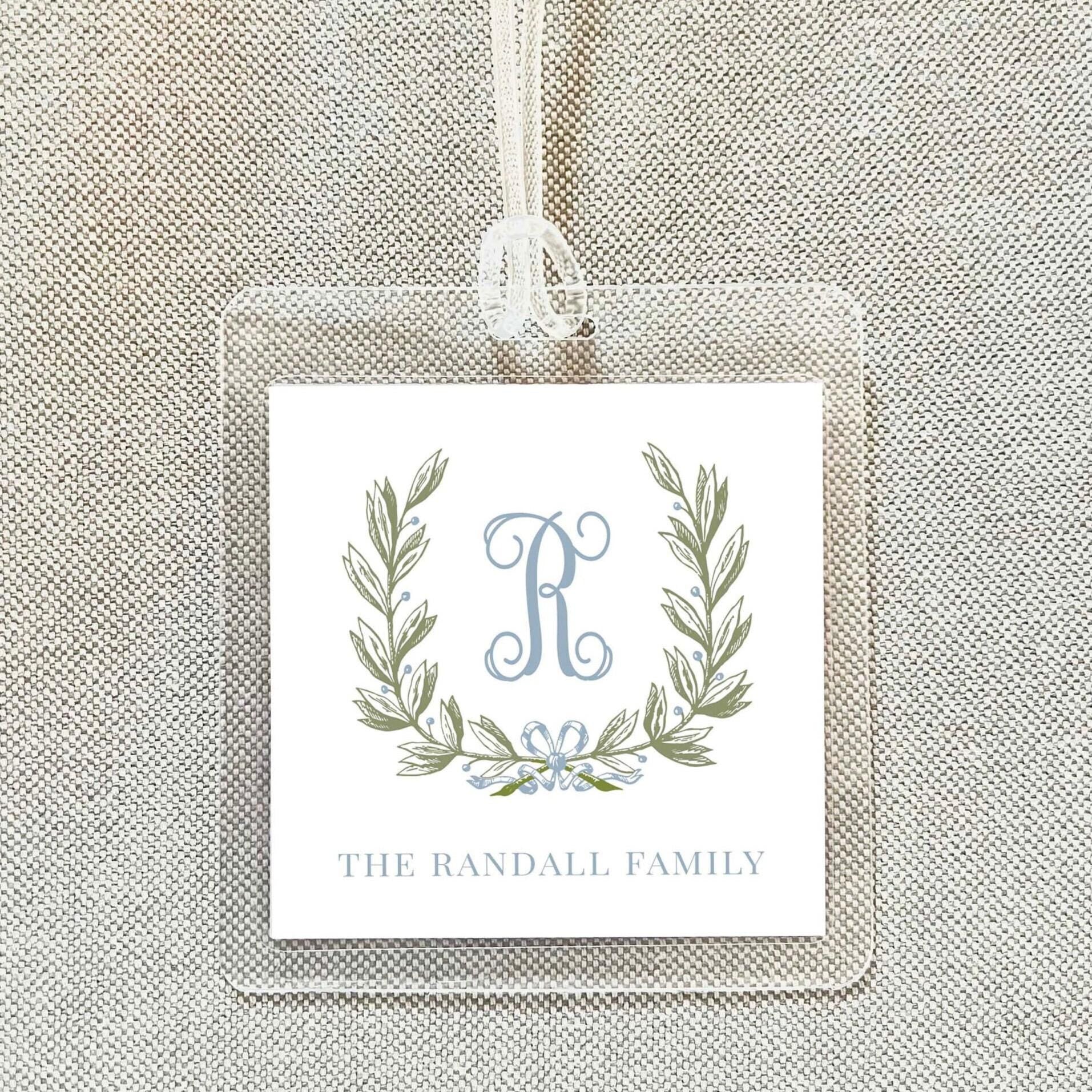 A clear plastic name tag with a monogrammed logo and text, hanging on a beige fabric background.