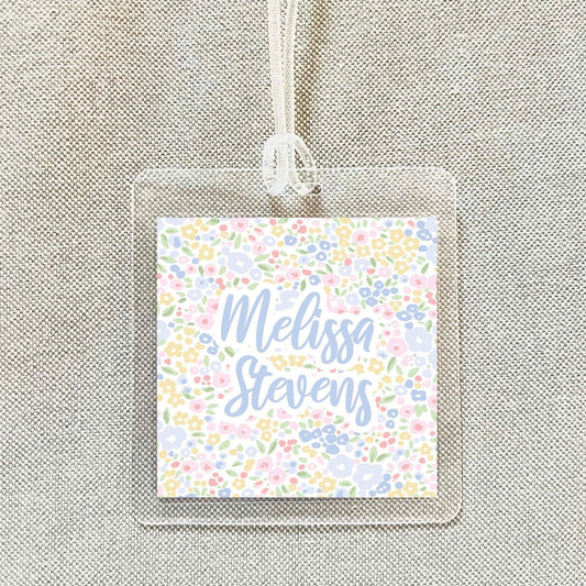 A clear plastic name tag with a floral design and the name "Melissa Stevens" printed on it.
