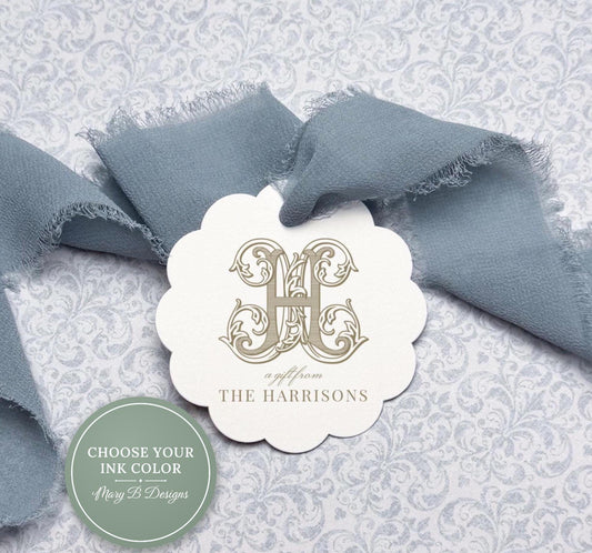 a white scalloped tag with a decorative monogrammed logo, placed on a gray and white floral background.