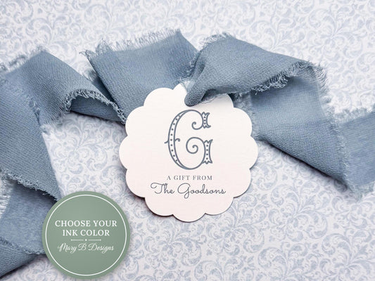 a white tag with a scalloped edge, placed on a gray and white floral background. The tag has a stylized letter "G" and the text "A Gift from The Goodsworths".