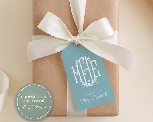 A gift box with a white ribbon and a blue tag that reads "MHE" is placed on a beige surface.