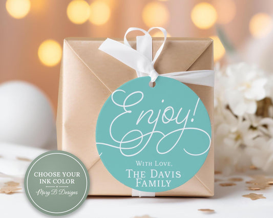 A gift box with a teal-colored circular tag that reads "Enjoy! With Love, The Davis Family" is placed on a table with white flowers and confetti.