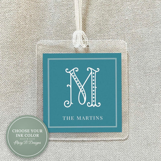 A square tag with a teal background and a white border, featuring a monogrammed letter "M" and the text "THE MARTINS" below it.