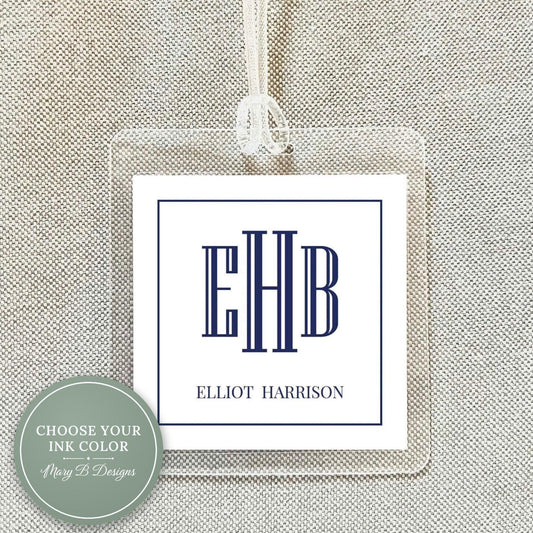 A clear plastic tag with a monogrammed logo and text, hanging on a fabric background.