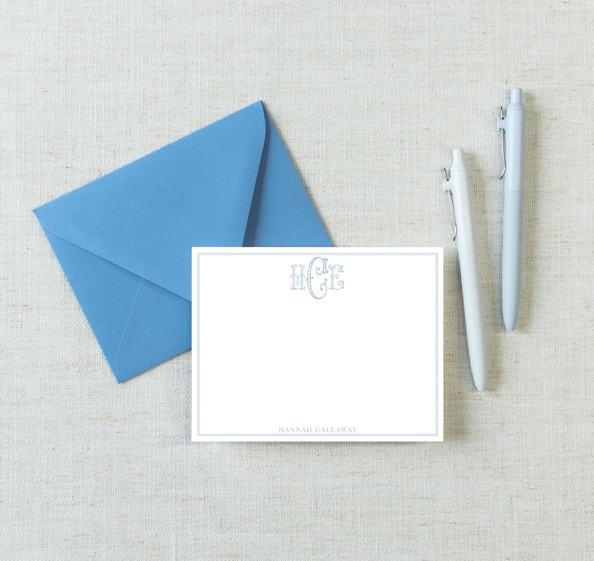 a blue envelope, a blank white card, and two pens arranged on a light-colored surface.
