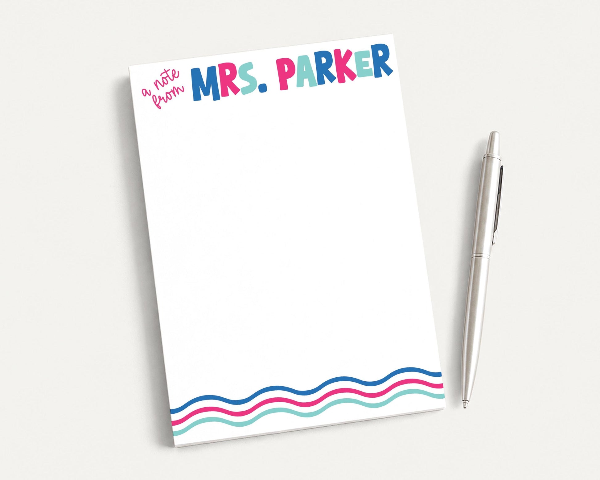 A blank notepad with the name "Mrs. Parker" written on it, along with a pen, is placed on a white surface.