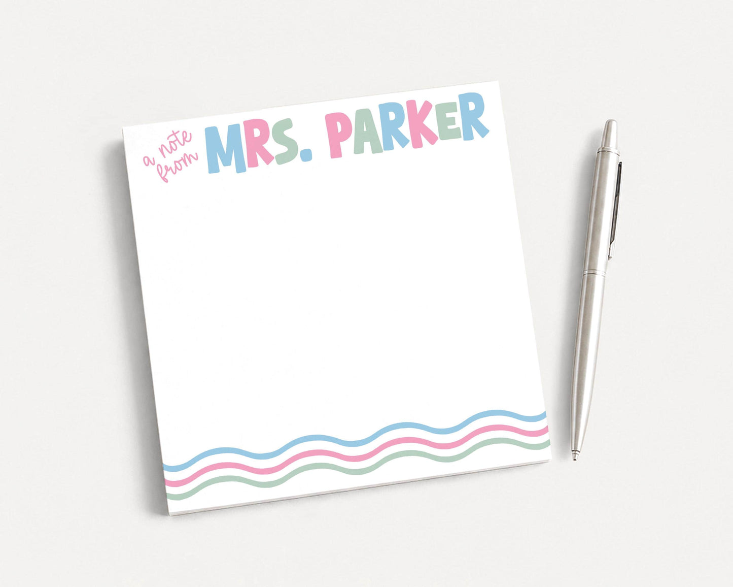 A white sticky note with the name "Mrs. Parker" written on it, along with a pen, is placed on a white surface.