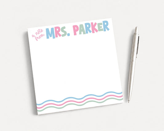 A white sticky note with the name "Mrs. Parker" written on it, along with a pen, is placed on a white surface.