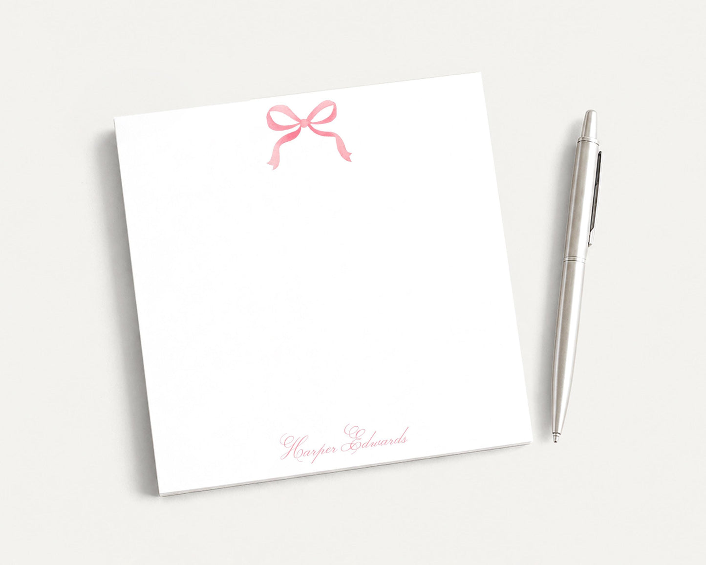 a white notepad with a pink bow and a pen on a plain white background.