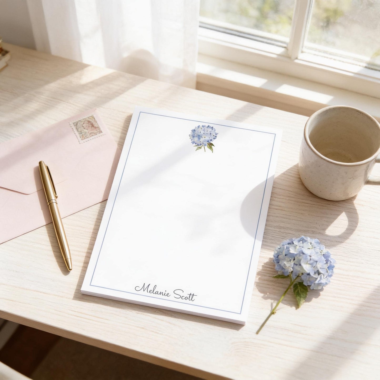 a desk with a blank card, a pen, a flower, and a cup of coffee.