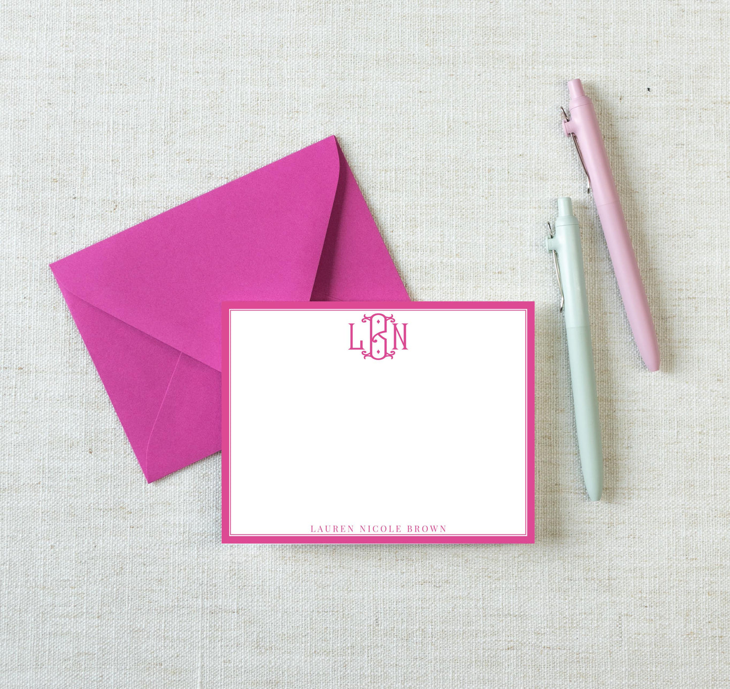 a pink envelope with a blank card inside, accompanied by two pens on a white background.