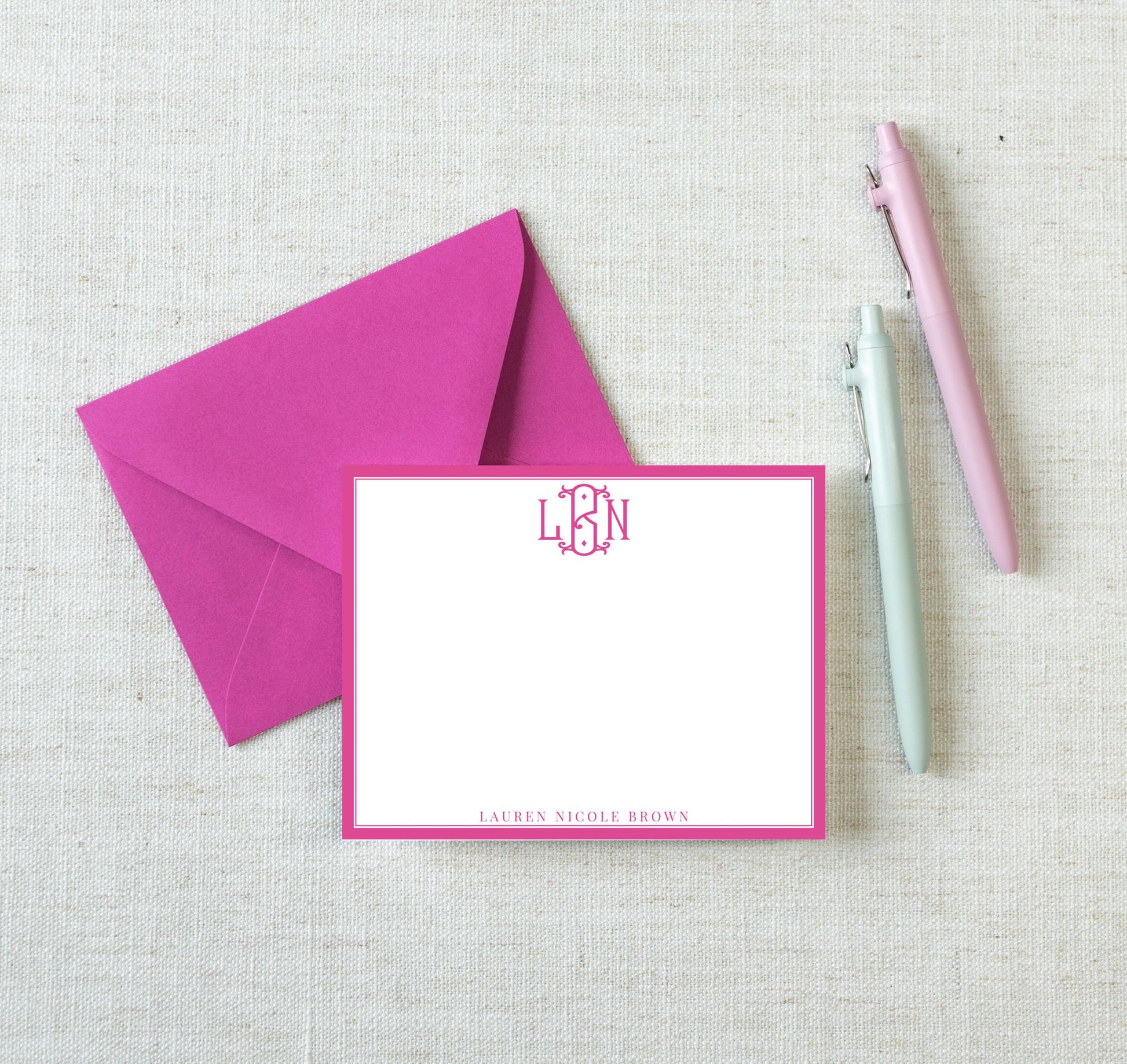 a pink envelope with a blank card inside, accompanied by two pens on a white background.