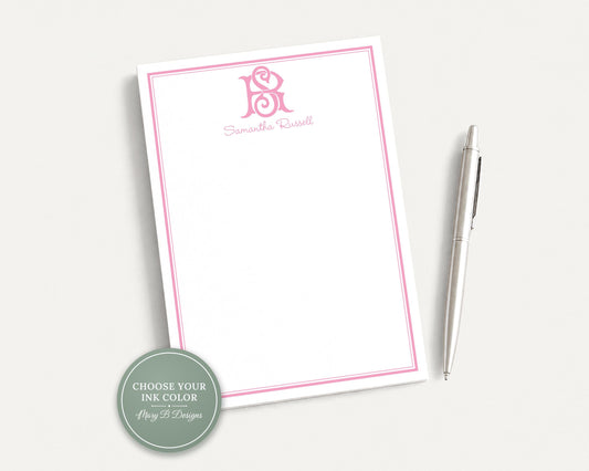 a pink-bordered, blank notepad with a pen resting on top of it.