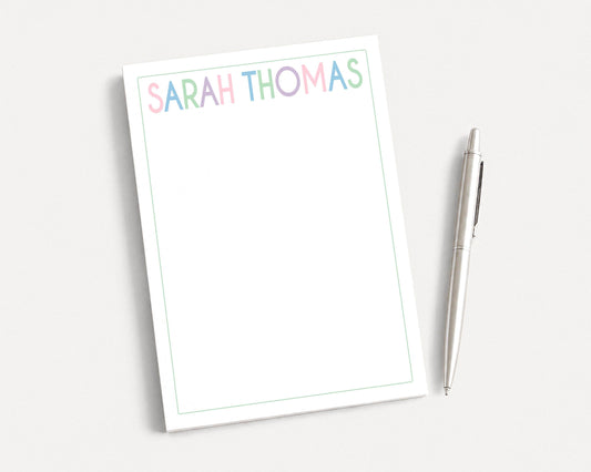 A blank white notepad with the name "SARAH THOMAS" written on it, along with a pen, is placed on a white surface.