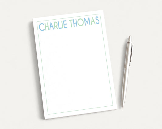 a blank white notepad with the name "CHARLIE THOMAS" written on it, accompanied by a silver pen.