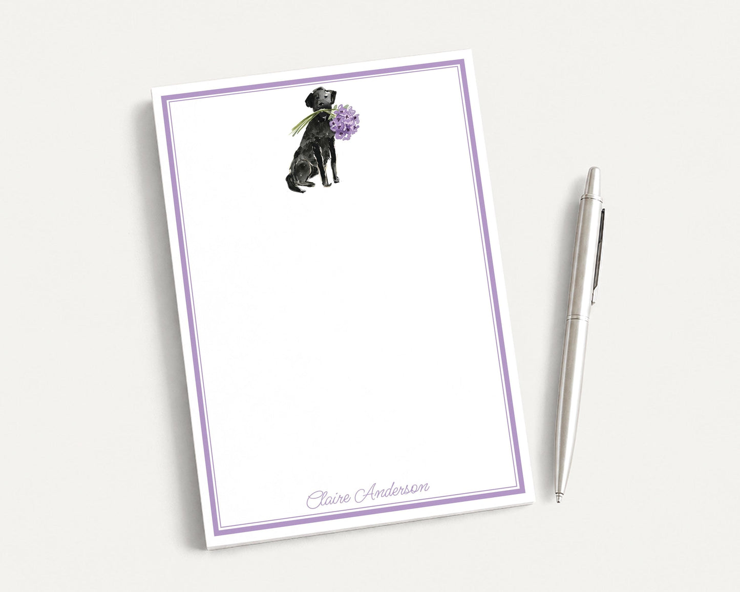 a blank notepad with a purple border, and a pen is placed next to it on a white surface.