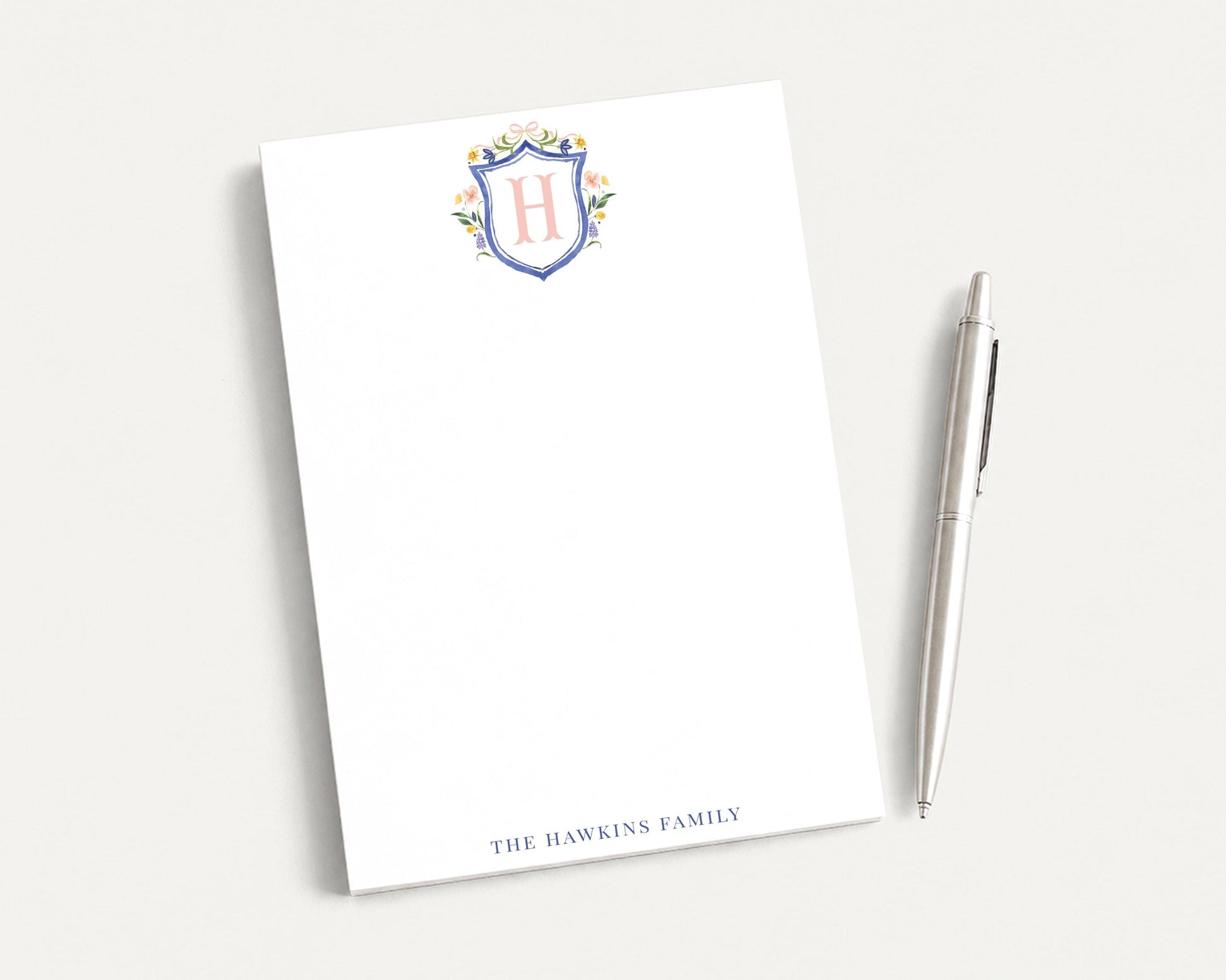 a blank white notepad with a pen next to it, both placed on a white surface.