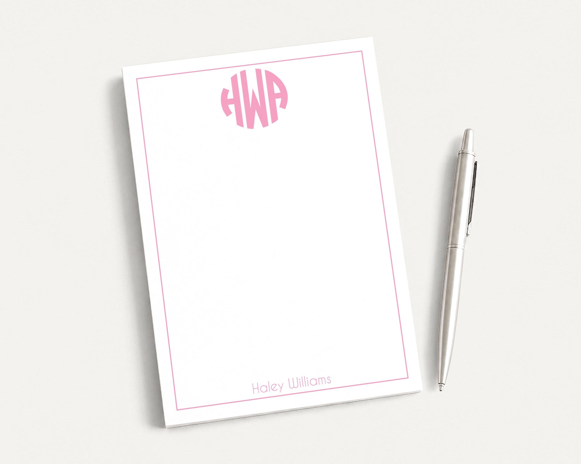 a white notepad with a pink border and a pen, both placed on a white surface.