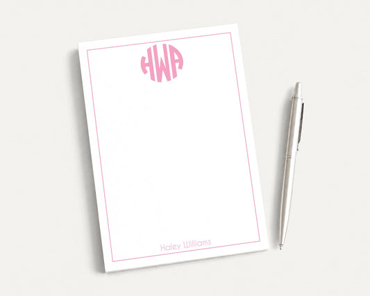a white notepad with a pink border and a pen, both placed on a white surface.